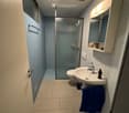 Modern bathroom with a white sink, toilet, glass shower enclosure, and built-in mirrored cabinet with shelves. Blue towel on the floor.