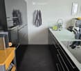 Modern kitchen with stainless steel appliances, white cabinets, and a light-colored countertop. Includes a sink, faucet, microwave, and various kitchen utensils.