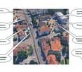 Aerial view of a residential area with multiple buildings, roads, and labeled points of interest such as a tram stop, restaurant, pharmacy, and hospital.