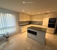Modern kitchen with white cabinets, stainless steel appliances, island with built-in oven, and a potted plant on the floor.
