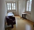 Office space with a brown leather chair, white desk, glass coffee table, and a small table near the window.