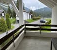 Balcony with a concrete floor, metal railing, and a view of a road, parked cars, and surrounding greenery.