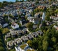Aerial view of a dense urban area with numerous buildings, including residential and commercial structures, surrounded by greenery and trees. The area features a mix of architectural styles, with some buildings equipped with solar panels on their rooftops