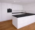 modern kitchen with white cabinets, black countertops, stainless steel oven, sink, faucet, wooden floor