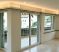 Empty room with large windows and sliding glass doors leading to a balcony. Light-colored tiled floor and white walls.