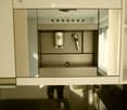 Modern kitchen with a built-in coffee machine featuring multiple buttons and a sleek design, integrated into white cabinetry.