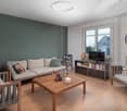 Modern living room with light wooden flooring, grey sectional sofa, wooden coffee table, and a TV stand with books and decorative items.
