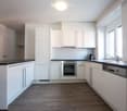 Modern kitchen with white cabinets, stainless steel appliances, dark countertops, and wooden flooring.