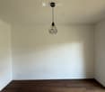 Empty room with wooden flooring, white walls, and a single hanging light fixture.