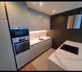 Modern kitchen with white cabinets, marble countertop, induction cooktop, stainless steel oven, and pendant lighting.