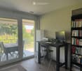 Bright room with a desk setup, a bookshelf, and a sliding glass door leading to a balcony.