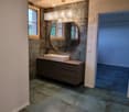 Modern bathroom with a dark grey cabinet, white sink, round mirror, and a chandelier above.