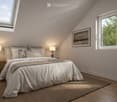Cozy attic bedroom with wooden floors, large windows, a neatly made bed, bedside tables with lamps, and a framed picture on the wall.