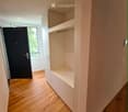 Modern hallway with wooden flooring, built-in white shelving unit, and a black door leading to a room with a window.