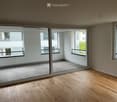 Empty room with wooden flooring, large sliding glass doors leading to a balcony area, and large windows providing natural light.
