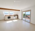 Modern kitchen with white cabinets, an oven, dishwasher, and a sink, featuring large windows and a sliding glass door leading to a balcony with a scenic view.