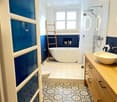 Modern bathroom with a freestanding bathtub, a sink with a wooden vanity, a toilet, a glass-enclosed shower, and a wooden ladder leaning against the wall. The walls are painted in a two-tone design with dark blue lower half and white upper half. The floor