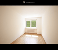 Empty room with wooden flooring, white walls, and a single window with a radiator below it.