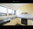 Modern kitchen with light-colored cabinets, black countertops, stainless steel sink, and built-in appliances including an oven and dishwasher. Large windows offer a scenic view.