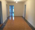 Empty hallway with tiled floor and white walls, featuring several doors and a visible room at the end.