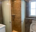 Modern bathroom with marble walls, a glass-enclosed shower stall, a toilet, and a sink.