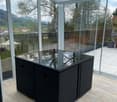 Glass-enclosed balcony with a wicker sofa, large windows offering a scenic view of the landscape.