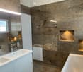 Modern bathroom with marble walls, a double sink, a bathtub, a large mirror, and built-in shelves.