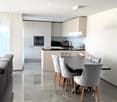 Modern dining area with a sleek black dining table and six upholstered chairs, adjacent to a contemporary kitchen with white cabinets, stainless steel appliances, and a polished tile floor.