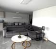 Modern living room with grey sectional sofa, white marble coffee table, side table, fan, and small plant. Open-plan layout includes a dining area with a table and chairs.