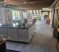 Open-plan kitchen and living area with wooden beams, grey cabinets, island, sink, coffee maker, and dining area with table and chairs.