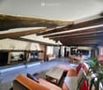 Open-plan living and dining area with exposed wooden beams, a fireplace, a sofa, a coffee table, a dining table with chairs, and a lamp.