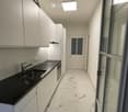 Modern kitchen with white cabinets, black countertop, stainless steel sink, and marble flooring.