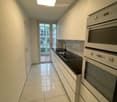 Modern kitchen with white cabinets, black countertops, a sink, and built-in oven. Large window offers a view of the balcony and outdoor area.