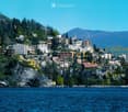 A scenic view of a town built on a hillside overlooking a lake, with numerous buildings and lush greenery.