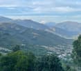 A panoramic view of a lush, green valley surrounded by mountains, with scattered houses and trees in the foreground.