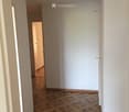 Empty hallway with wooden flooring and white walls, featuring two doors and a visible room at the end.
