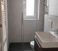 Modern bathroom with dark tiled floor, white sink, toilet, glass shower enclosure, and radiator.