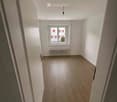 Empty room with wooden flooring, white walls, a single window, and a radiator below it. No furniture or personal items are present.