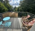 Balcony with a turquoise table, two turquoise chairs, and two wooden deck chairs with patterned cushions, surrounded by a metal railing and bamboo screen.