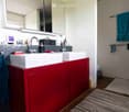 Modern bathroom with double sinks, red cabinet, large mirror, and towels hanging on racks.