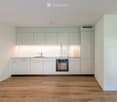 Modern kitchen with light grey cabinets, a stainless steel oven, a sink with a faucet, and a light wooden floor.