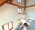 Spacious hallway with white textured walls, wooden beams, multiple windows, and a staircase leading upwards.