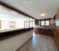 Empty kitchen with wooden cabinets, tiled floor, and large windows. No furniture or appliances are present.