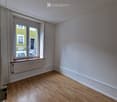 Empty room with light wooden flooring, white walls, and a large window with a radiator below it.