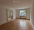 Empty room with wooden flooring, large window, and double doors leading to another space.