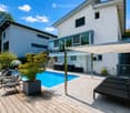 Modern two-story house with a swimming pool, lounge chairs, and a covered patio area.