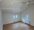 Empty room with wooden flooring, white walls, and a ceiling fan. Two windows provide natural light, and radiators are installed under the windows.