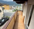 Balcony with wooden decking and railing, overlooking a street with a parked car and distant mountains.