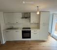 Modern kitchen with white cabinets, stainless steel appliances, and wooden flooring. Features an induction cooktop, oven, sink, and range hood.