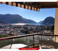 Balcony with a panoramic view of a cityscape, lake, and mountains under a clear blue sky.